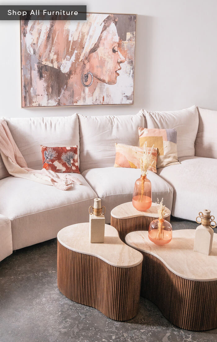 A cozy living room with a beige sectional sofa, colorful pillows, wooden coffee tables, and an abstract painting on the wall.